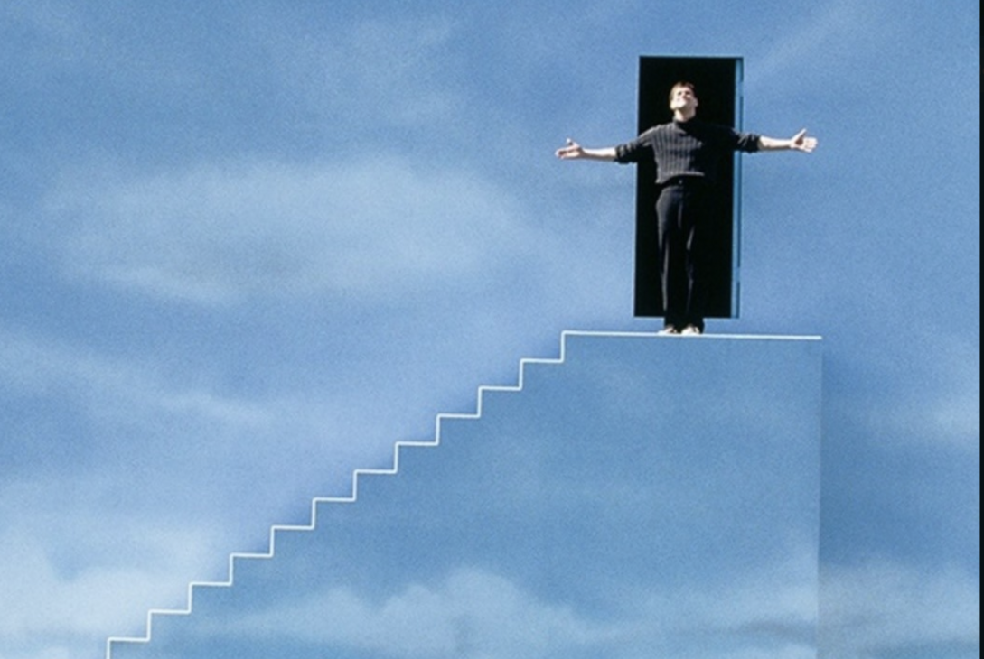 man coming out of doorway to stand on steps, with a background of clouds on the wall,and looking up at sky